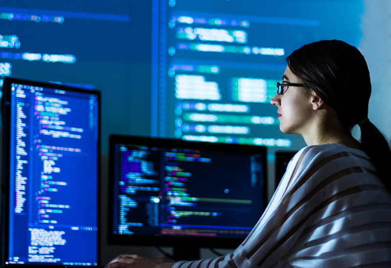 Female software developer writing code in a room with computer monitors.
