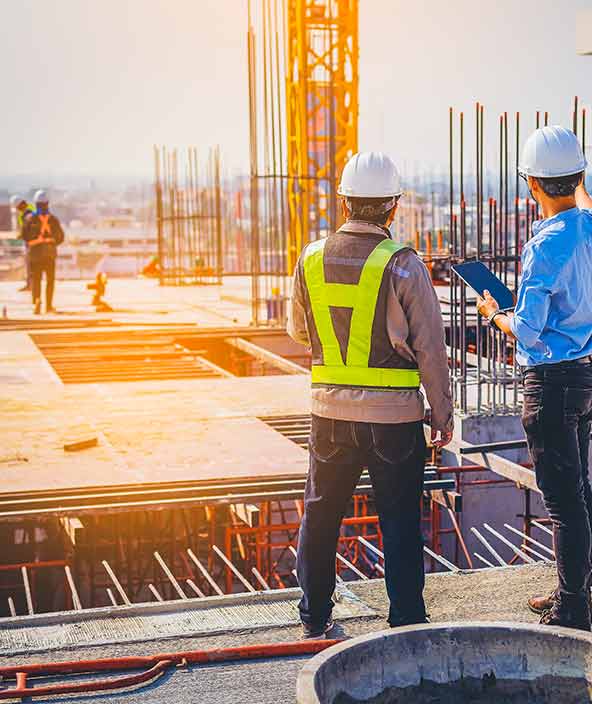 Un empleado de construcción visualizando datos en una tableta y de pie frente a un proyecto de construcción y otros empleados