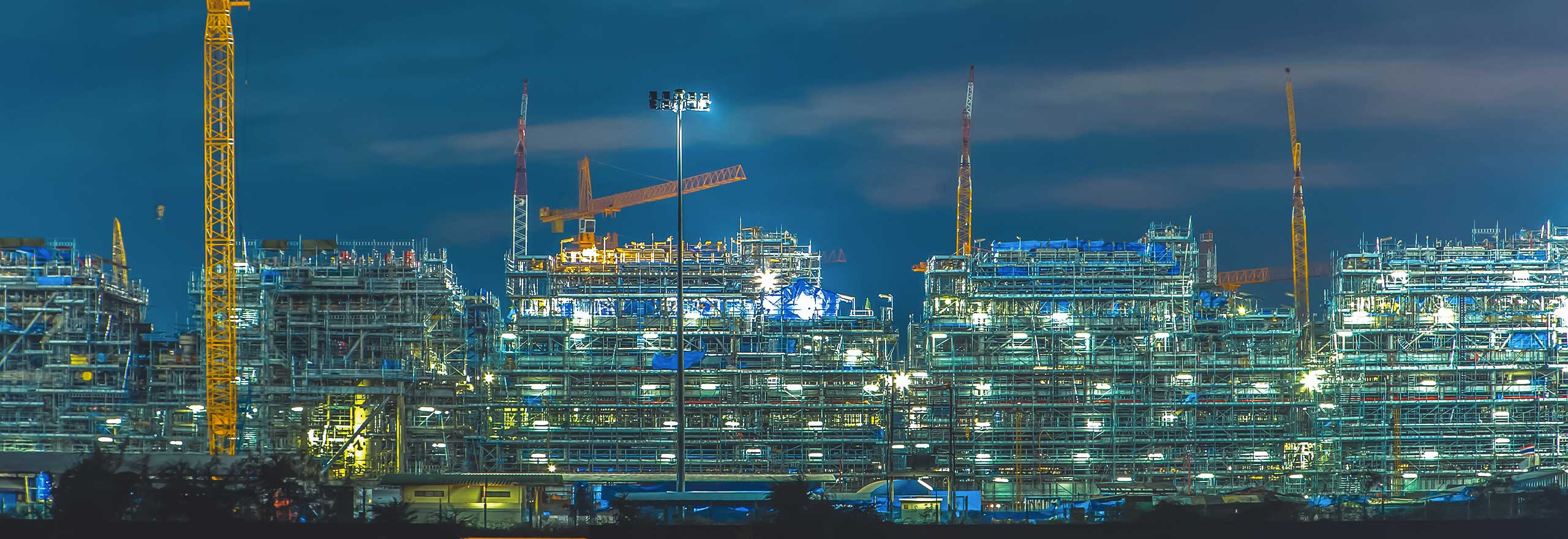 A wide shot of a large construction site and multiple cranes at night