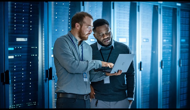 Two men looking at a laptop in a data center and/or server farm.