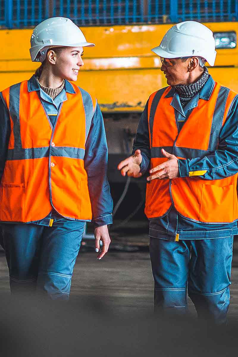 Due dipendenti che indossano elmetti e giubbotti di sicurezza dai colori vivaci che parlano all'aperto