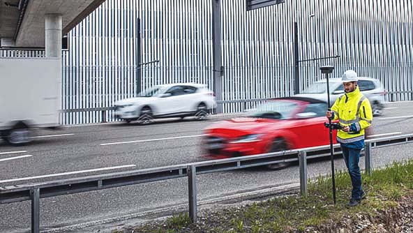  A man in a yellow jacket stands by the roadside, showcasing the importance of precision in GNSS positioning tasks.