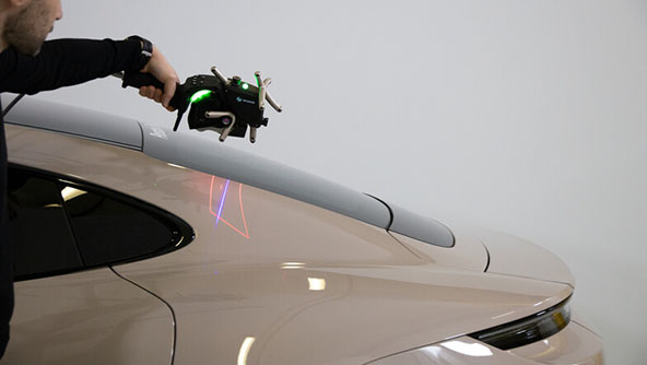 Image of person using hand held 3D scanner near the rear view window on a car