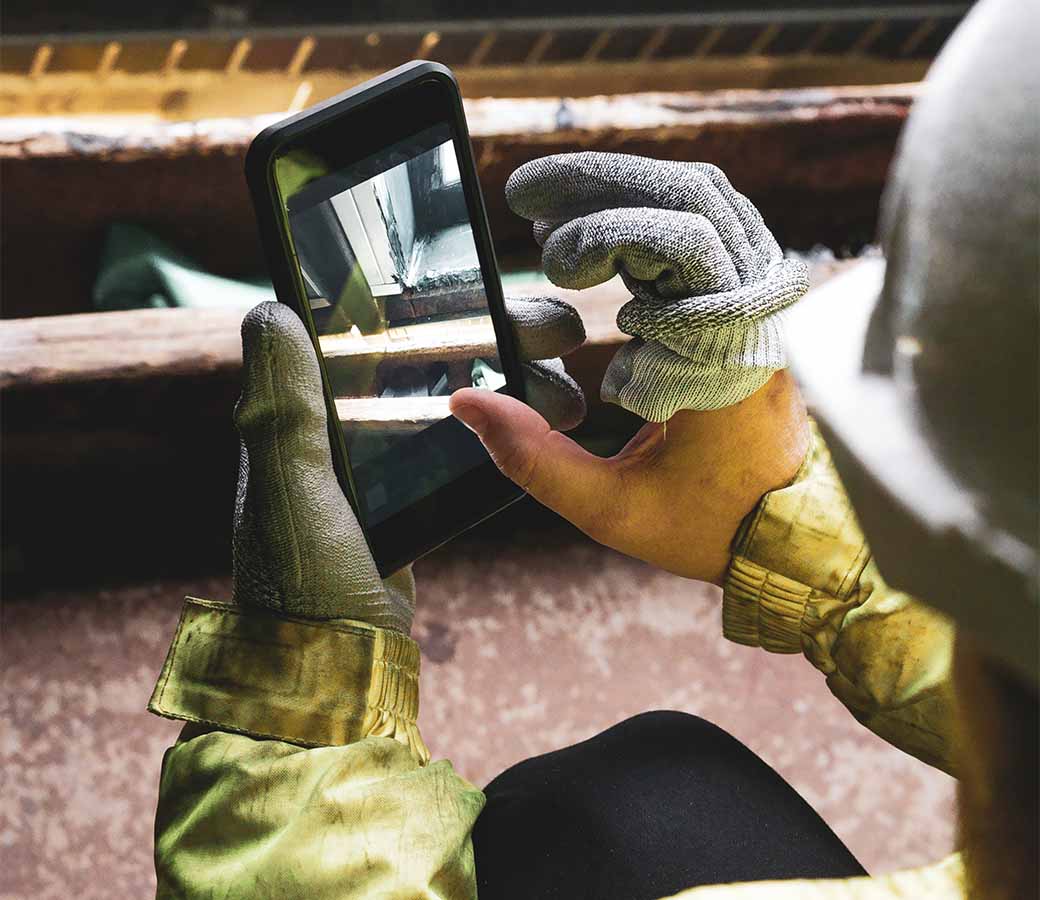 Young architect holding a mobile device on a construction site to submit an incident report.