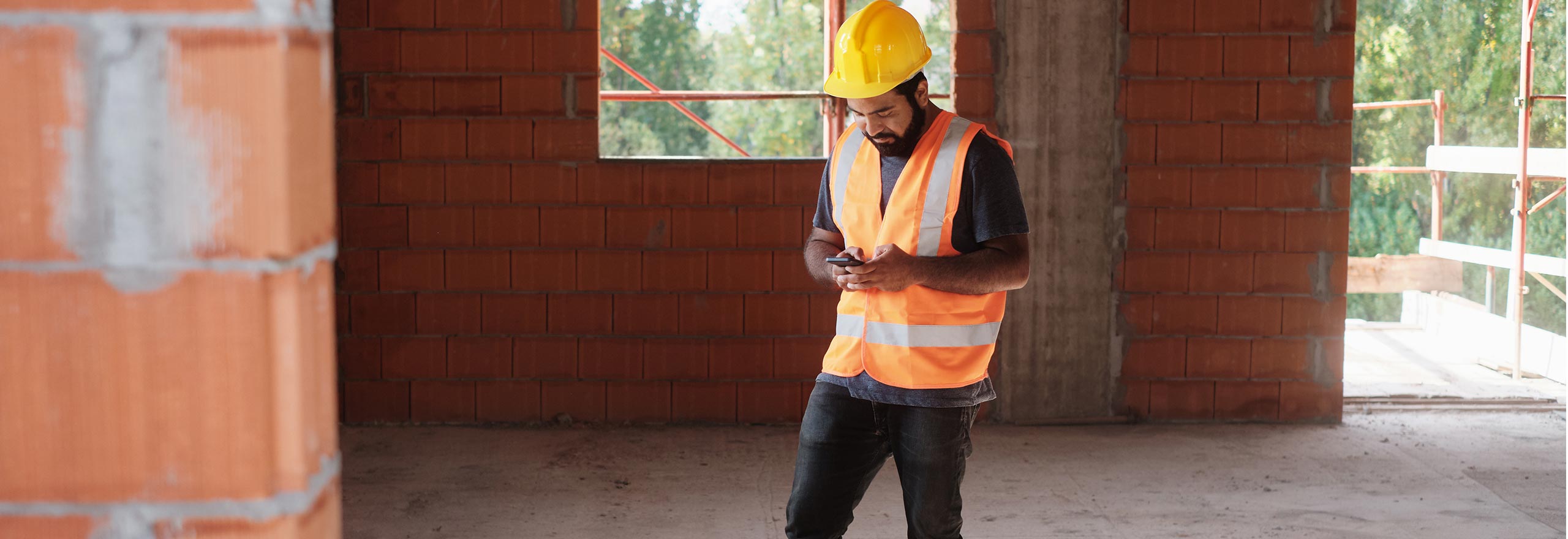 Man at work on construction site using a mobile device for message and communications about safety procedures