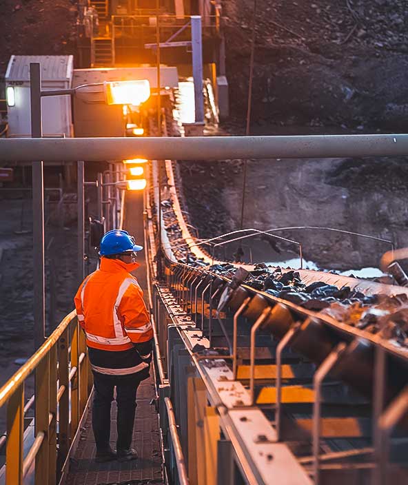 Shallow depth of field image of a miner inspecting ore rocks on a conveyor